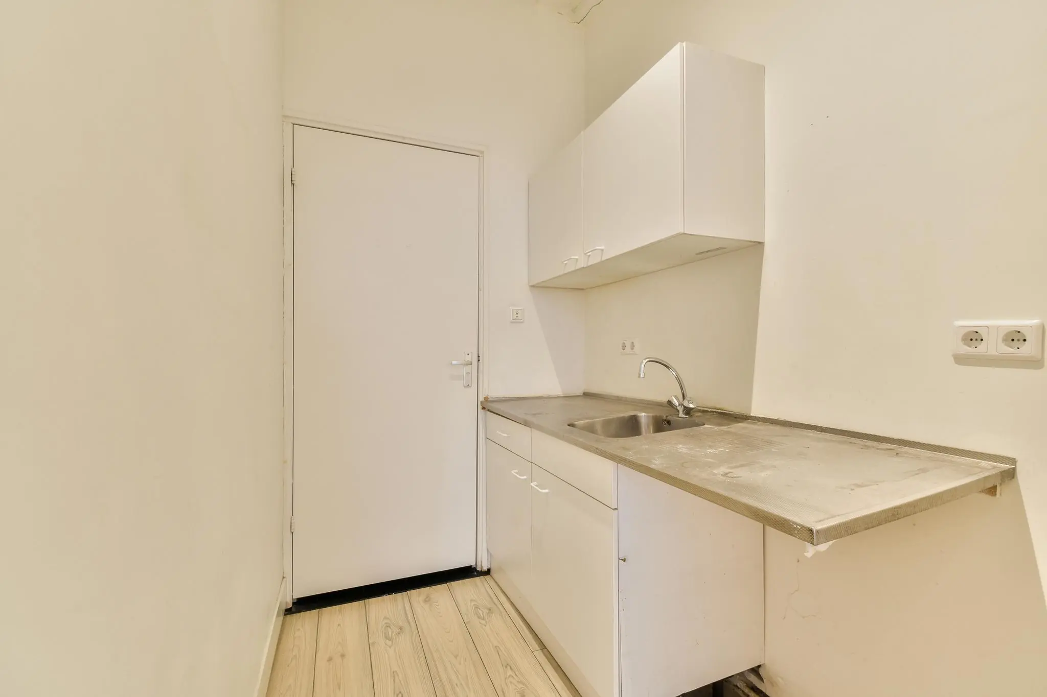 Kleine, eenvoudige keuken aan de Korte Schimmelstraat met wit aanrecht, gootsteen en bovenkastjes.